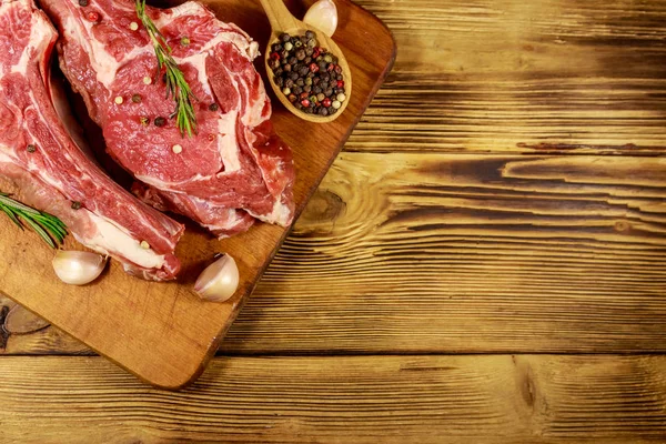 Raw fresh beef rib eye steak on bone with spices, garlic and rosemary on wooden table. Top view — Stock Photo, Image