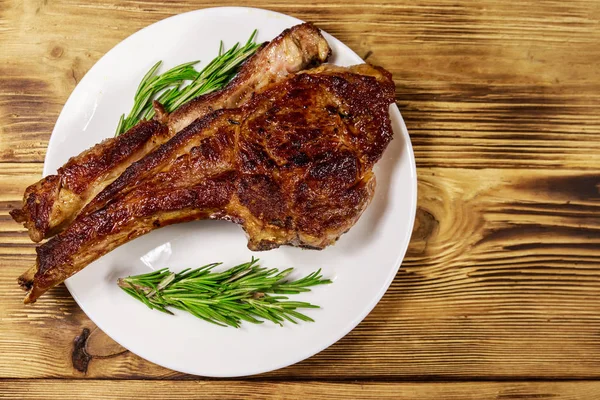 Roasted beef rib eye steak on bone with rosemary in white plate
