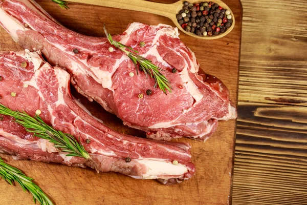 Kemiğin üzerinde çiğ biftek, baharatlar ve ahşap masada biberiye. Üst görünüm — Stok fotoğraf