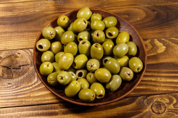 Тарелка с зелеными оливками на деревянном столе — стоковое фото
