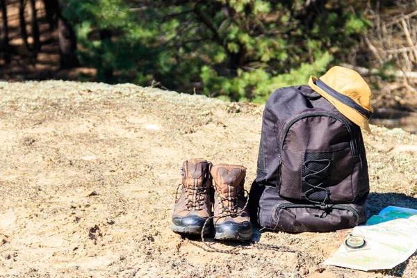 Tourist backpack with hiking boots, hat, compass and map on the glade in pine forest. Trekking hike gear equipment. Travel concept — Stock Photo, Image