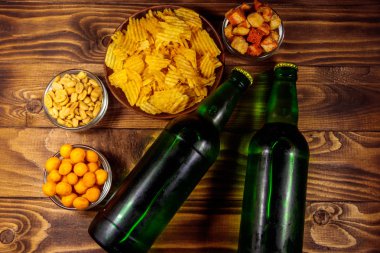Bira şişeleri ve ahşap masada bira için çeşitli atıştırmalıklar.