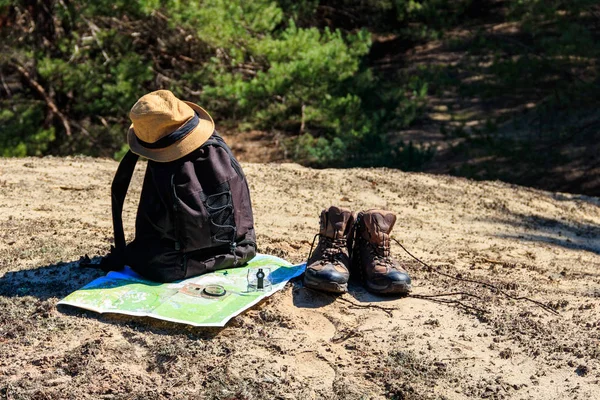 Tourist backpack with hiking boots, hat, compass and map on the glade in pine forest. Trekking hike gear equipment. Travel concept — Stock Photo, Image