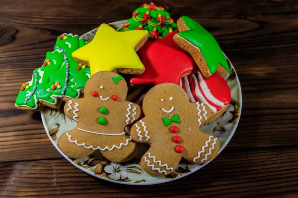 จานที่มีคุกกี้ขนมปังขิงเทศกาลคริสต์มาสอร่อยในรูปต้นคริสต์มาส ชายขนมปังขิง ดาวและถุงเท้าคริสต์มาสบนโต๊ะไม้ — ภาพถ่ายสต็อก