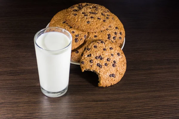 Ciasteczka czekoladowe i szklanka mleka na drewnianym stole — Zdjęcie stockowe