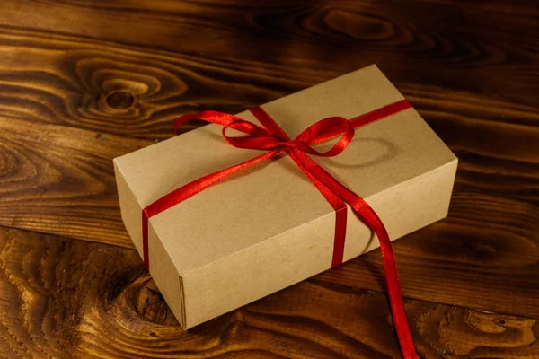 Tekturowe pudełko z czerwoną wstążką na drewnianym stole — Zdjęcie stockowe