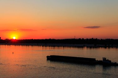 Römorkör, gün batımında Dinyeper nehrinde ağır, uzun bir mavnayı itiyor.