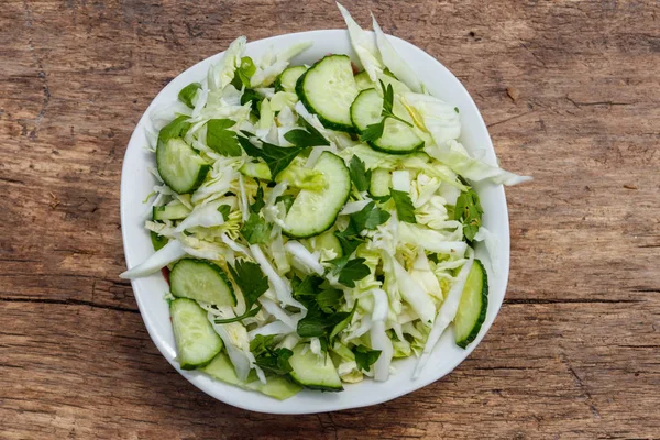 Tavaszi vegán saláta, káposzta, uborka, zöld hagyma, petrezselyem a fából készült asztal. Szemközti nézet — Stock Fotó