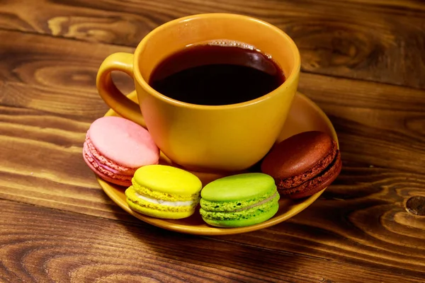 Tasse Kaffee mit leckeren bunten Macarons auf Holztisch — Stockfoto