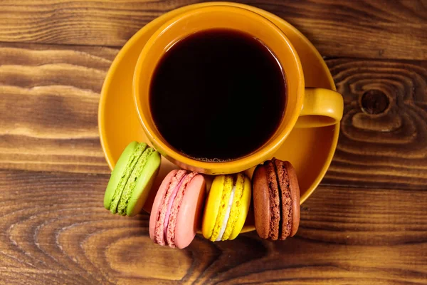 Taza de café con sabrosos macarrones de colores en la mesa de madera. Vista superior — Foto de Stock