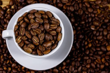 Kahve çekirdekleri arka planda beyaz fincan kavrulmuş kahve çekirdekleri. Üstte görüntü