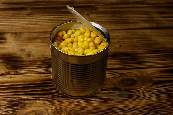 Open tin can of corn on wooden table — Stock Photo, Image