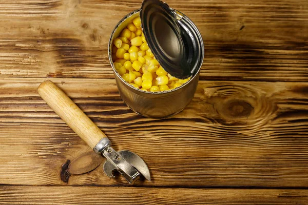 Open tin can of corn and can opener on wooden table — Stock Photo, Image