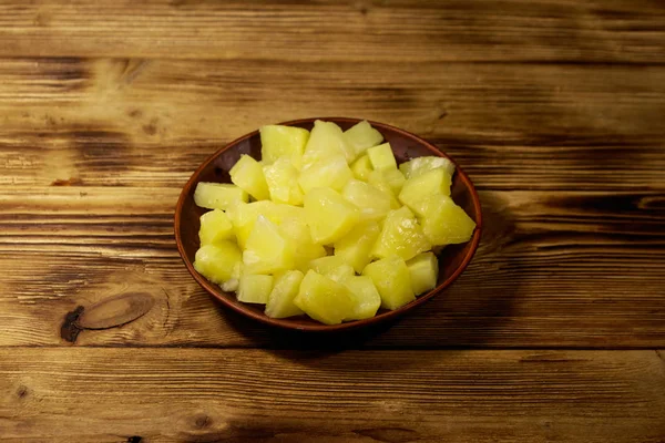 Canned pineapple pieces in ceramic plate on wooden table