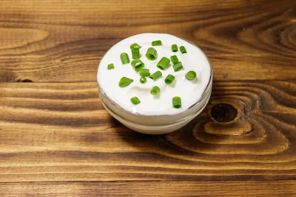 Crema agria con cebolla verde en cuenco de vidrio sobre mesa de madera —  Fotos de Stock