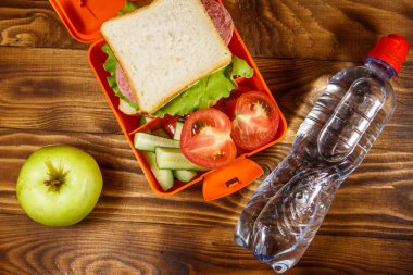 Sandviç ve taze sebze, su şişesi ve ahşap masa üzerinde yeşil elma ile Okul öğle yemeği kutusu. Sağlıklı beslenme konsepti. Üstte görüntü