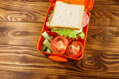 Sandviç ve ahşap masa üzerinde taze sebze ile okul beslenme çantası. Üstten görünüm