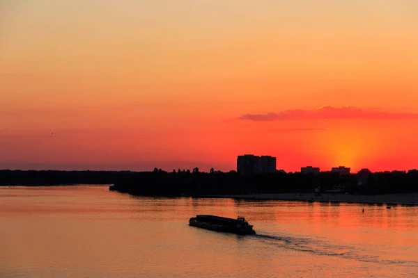 Tugboat duwt een zware lange boot op de rivier de Dnjepr bij zonsondergang — Stockfoto
