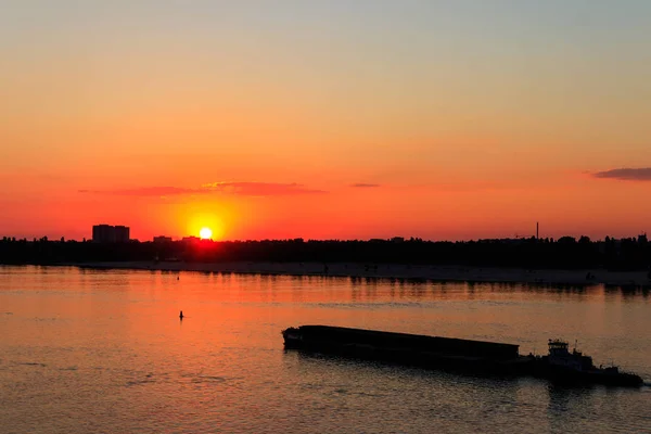 Tugboat pushing a heavy long barge on the river Dnieper at sunset Stock Photo