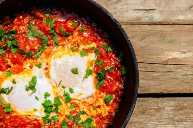 Ev yapımı kahvaltı shakshuka - kızarmış yumurta, soğan, biber, domates ve maydanoz rustik ahşap masa üzerinde dökme demir tavada. Yahudi mutfağı. Üstten görünüm
