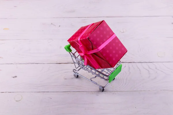 Shopping cart with big gift box on white wooden background — Stock Photo, Image