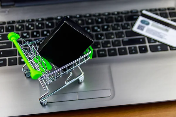 Concepto de compras online. Pequeño carrito de compras con caja y tarjeta de crédito en el teclado portátil —  Fotos de Stock