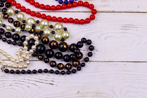 Different beads necklaces on white wooden background