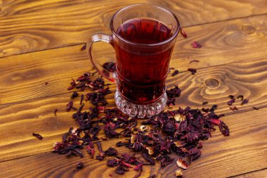 Ahşap masada bir bardak kırmızı amber çayı (carcade, roselle).