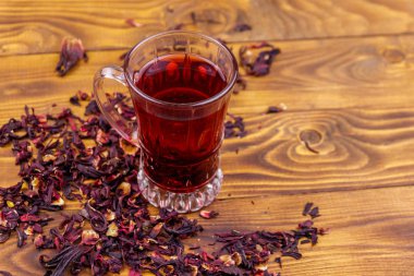 Ahşap masada bir bardak kırmızı amber çayı (carcade, roselle).