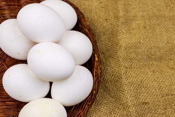 White chicken eggs in wicker basket on sackcloth background — Stock Photo, Image