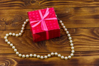 Ahşap arka planda hediye kutusu ve inci kolye.