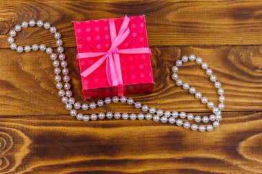 Ahşap arka planda hediye kutusu ve inci kolye.