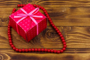 Ahşap arka plan üzerinde hediye kutusu ve kırmızı boncuk kolye