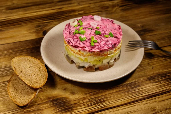 Salată tradițională rusă "Herring sub o haină de blană" (shuba) pe masă de lemn. Salată stratificată cu hering, sfeclă, morcovi, ceapă, cartofi și ouă — Fotografie, imagine de stoc