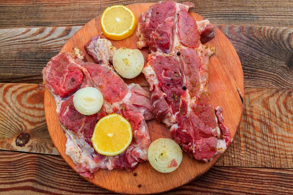 Carne fresca de cerdo cruda con especias, limón y cebolla sobre tabla de cortar de madera sobre mesa rústica. Vista superior —  Fotos de Stock