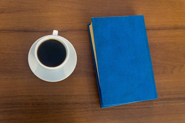 Taza de café y libro cerrado sobre mesa de madera — Foto de Stock