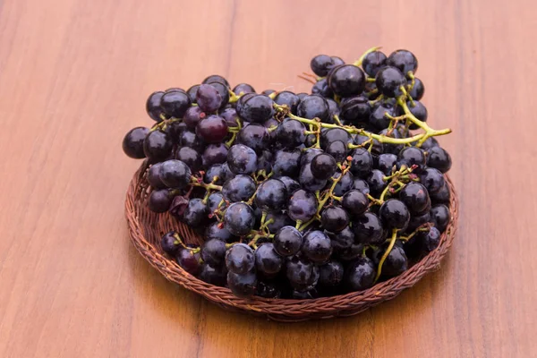 Ripe grapes in wicker basket on wooden table — Stock Photo, Image
