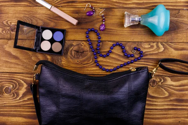 Damenaccessoires auf Holzgrund. Clutch Tasche, Flasche Parfüm, Lidschatten, Halskette und Ohrringe auf dem Holztisch. Schönheit und Modekomposition. Draufsicht, flache Lage — Stockfoto