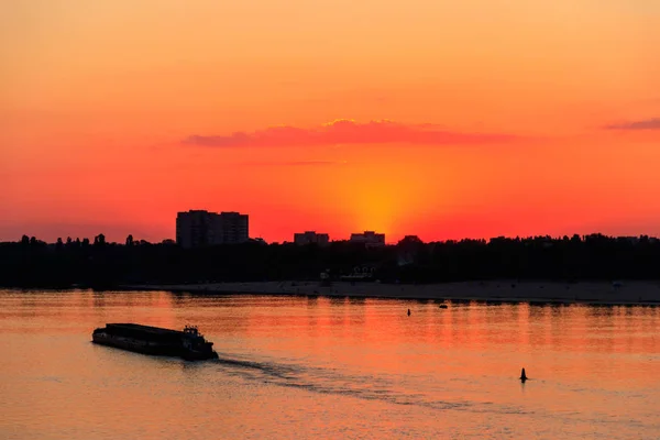 Tugboat duwt een zware lange boot op de rivier de Dnjepr bij zonsondergang — Stockfoto