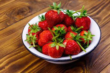 Tahta bir masada beyaz kasede taze olgun çilek.