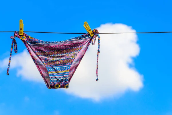 Traje de baño femenino de secado colgado de una cuerda contra el cielo azul — Foto de Stock