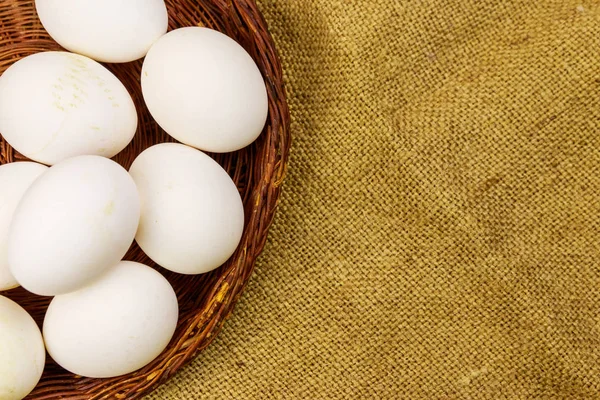 White chicken eggs in wicker basket on sackcloth background — Stock Photo, Image