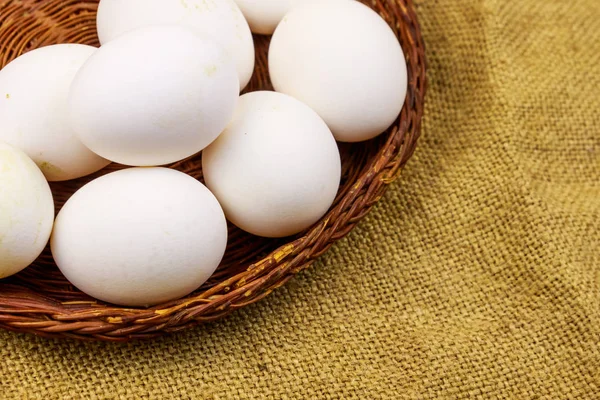 White chicken eggs in wicker basket on sackcloth background — Stock Photo, Image