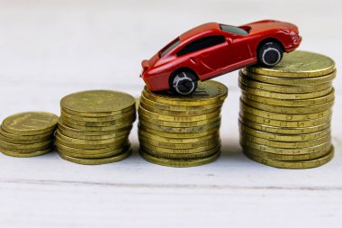 Beyaz ahşap arka plan üzerinde altın sikke yığınları üzerinde Minyatür araba modeli