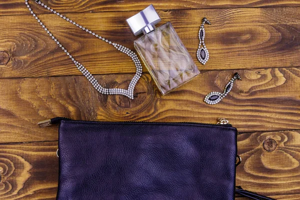 Damenaccessoires auf Holzgrund. Clutch Bag, eine Flasche Parfüm, Halskette und Ohrringe auf einem Holztisch. Schönheit und Modekomposition. Draufsicht, flache Lage — Stockfoto