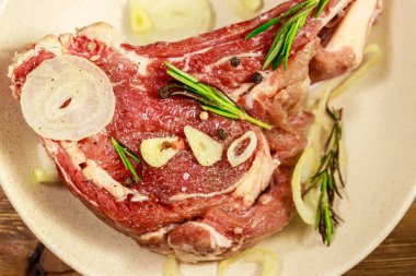 Kemik üzerinde marine edilmiş biftek, baharat, soğan ve ahşap masada biberiye.