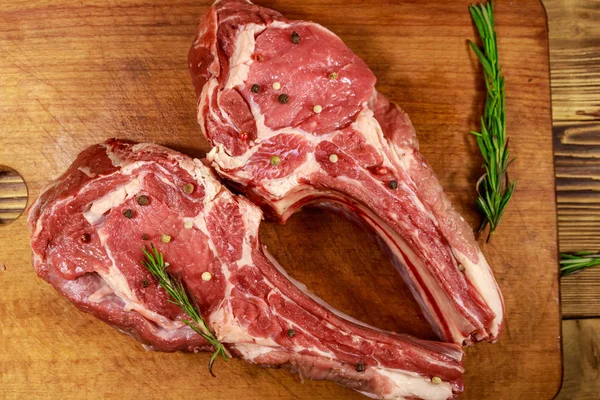 Raw fresh beef rib eye steaks on bone with spices and rosemary on wooden table. Top view