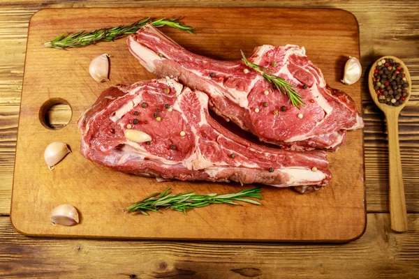 Raw fresh beef rib eye steak on bone with spices, garlic and rosemary on wooden table. Top view — Stock Photo, Image