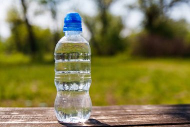 Doğanın arka planında, ahşap bir masanın üzerinde taze içme suyu olan plastik şişe.