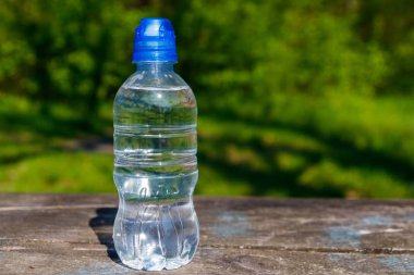 Doğanın arka planında, ahşap bir masanın üzerinde taze içme suyu olan plastik şişe.